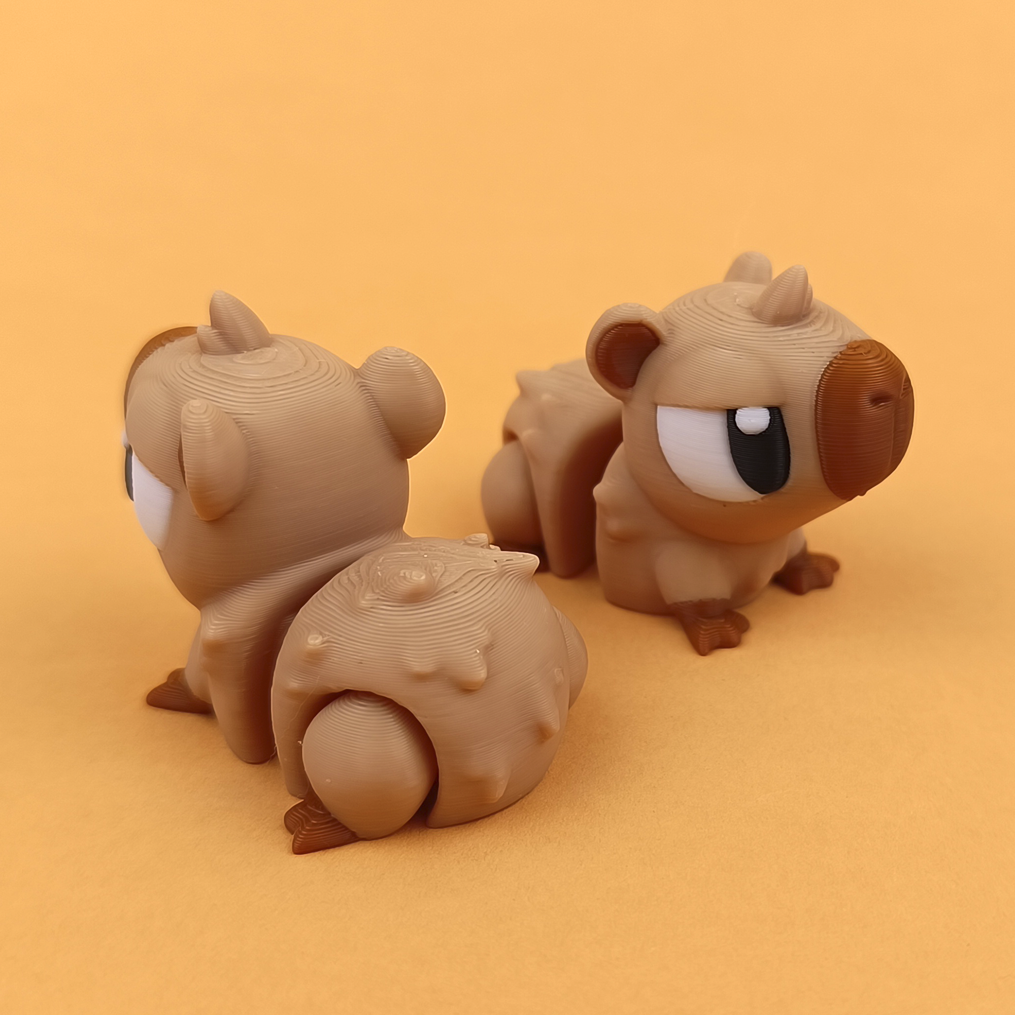 3D-gedruckte Printimon-Figur: zwei kleine Wasserschwein-Babys mit großen Kulleraugen auf warmem orangefarbenem Hintergrund.